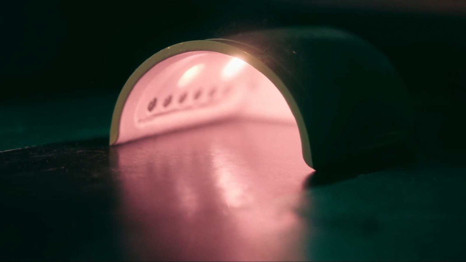 The soft rose glow of a curing lamp on a dark salon table