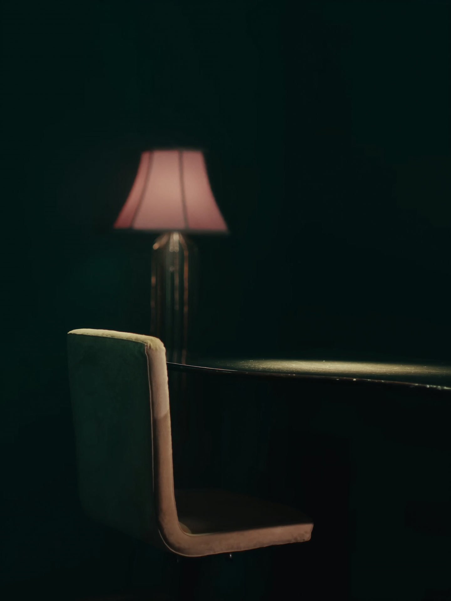 An empty chair at a salon table, lit by a soft rose lamp